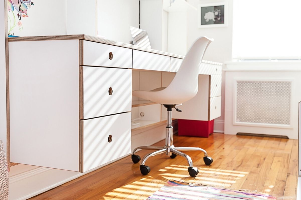 Sunny room with wooden floor, white desk, chair, and colorful rug.