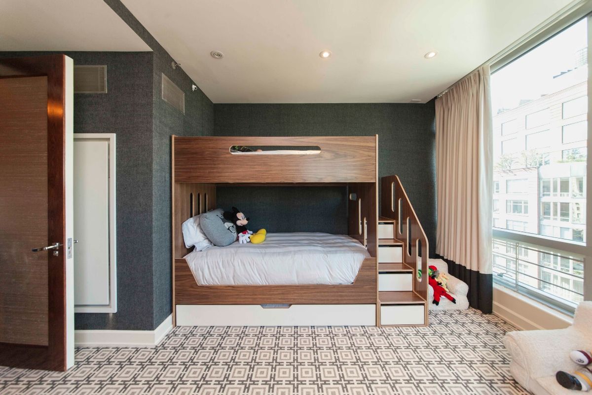 Modern hotel room with a bunk bed and plush toys, featuring a large window and geometric carpet.