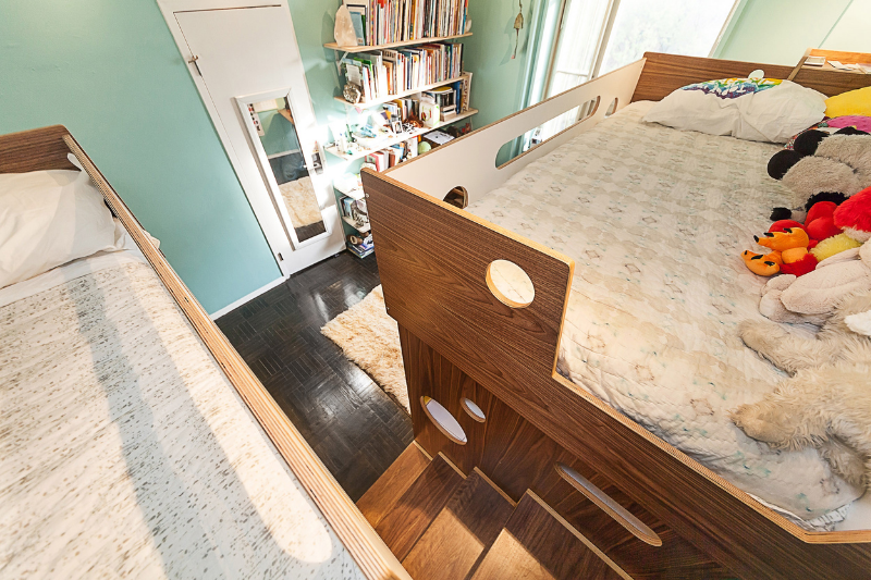 Elevated children's bed with built-in storage in a bright room with wooden flooring and toys.