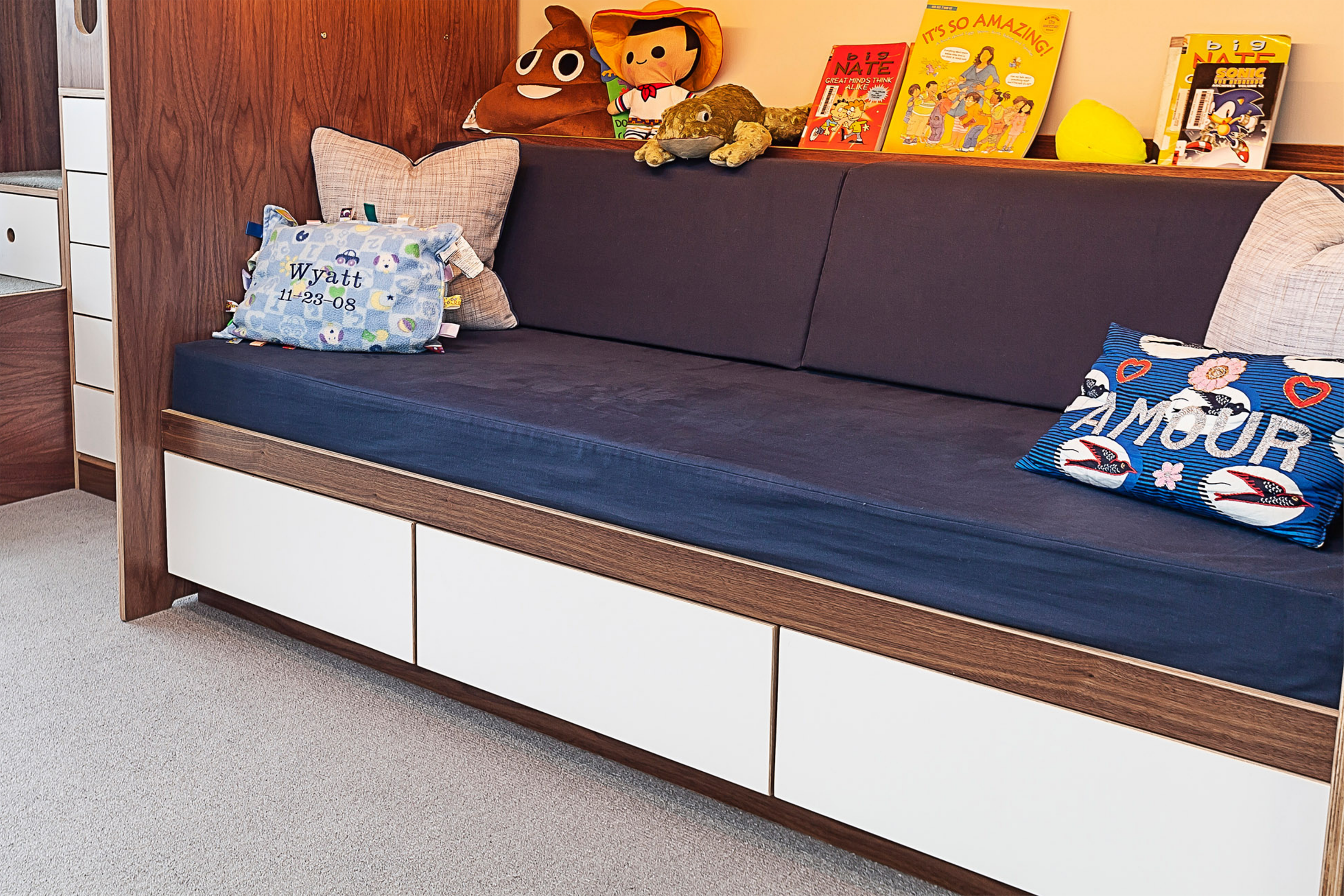 Cozy children's reading nook with a dark blue sofa, colorful pillows, and books on display.