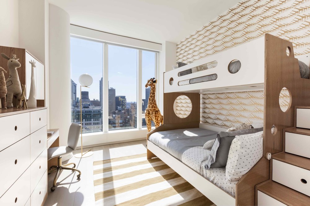 Modern sunny bedroom with bunk beds, city view, striped rug, and wooden furniture.