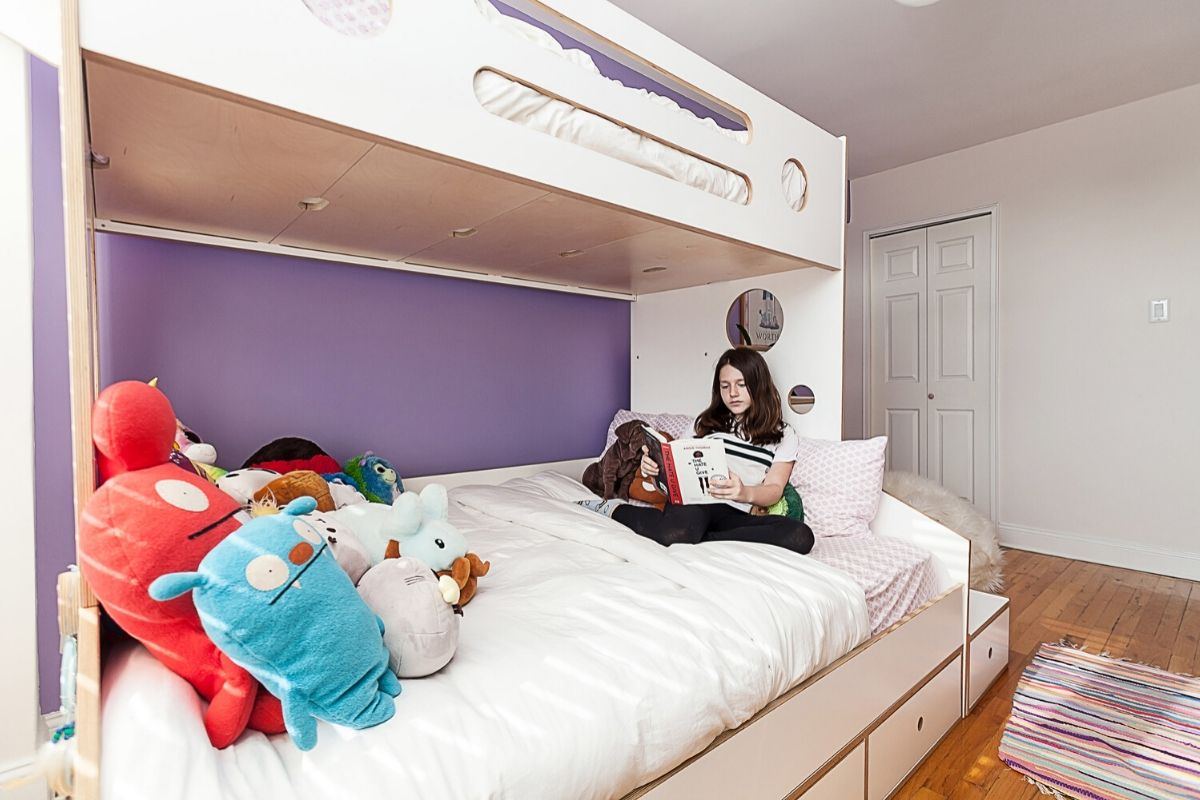 Person on bed reading, surrounded by plush toys, purple wall.