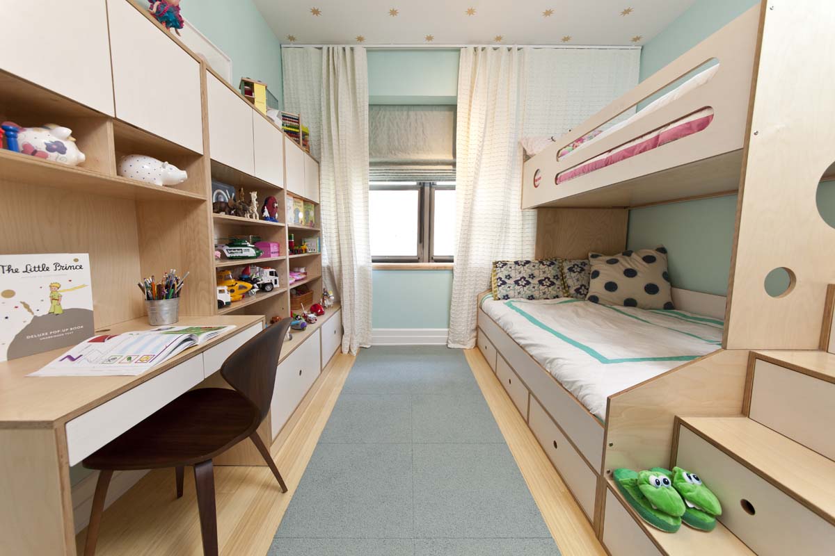 Bright children's room with built-in bunk beds, study area, and shelves full of toys and books.