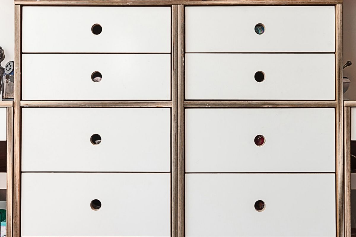 Wooden chest with nine white drawers and varied knobs.