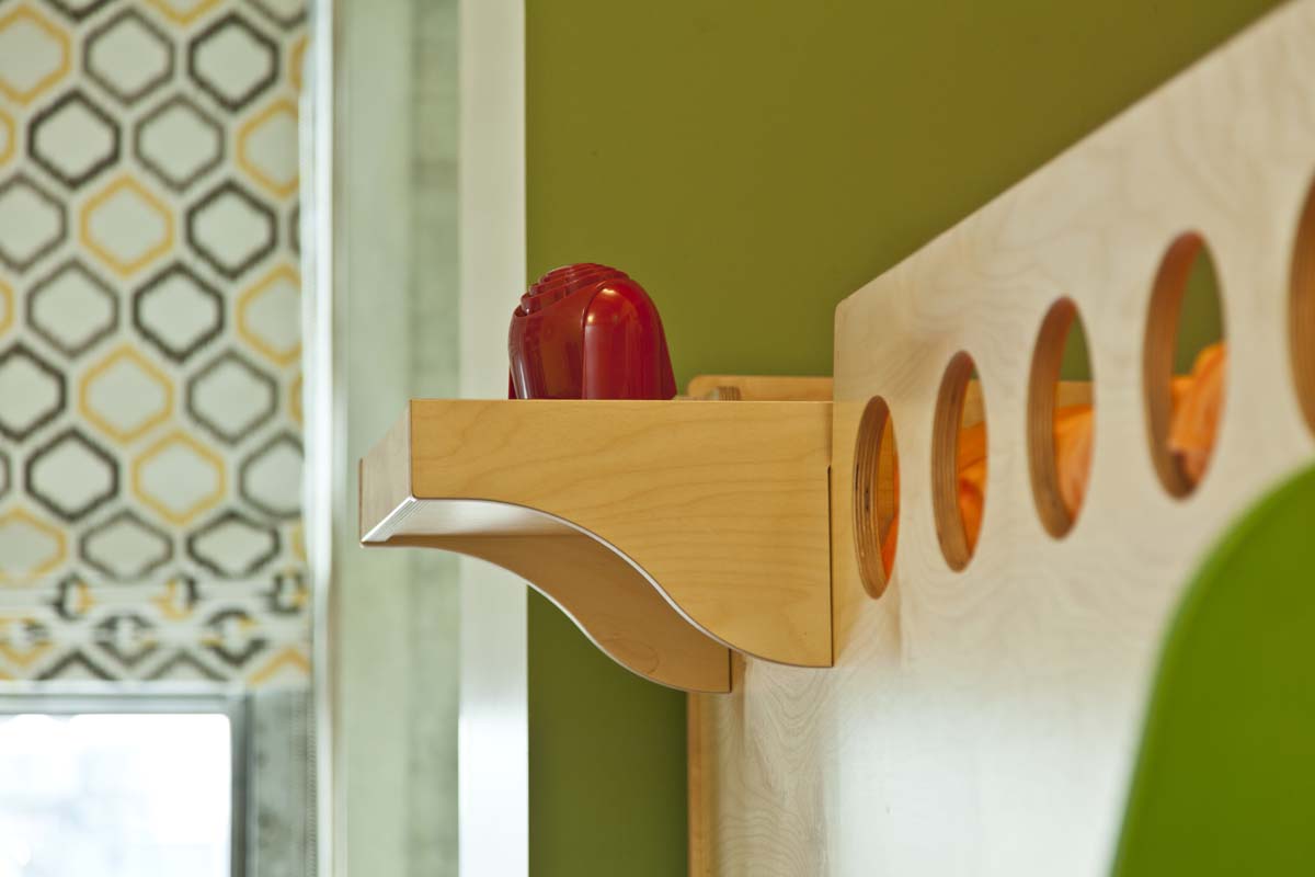 Wooden shelf with circular cutouts, red object, against a green wall.