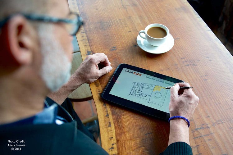 Man with glasses using tablet, coffee cup, ruler on table.