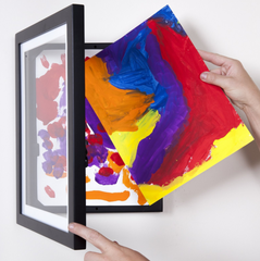Hand framing vibrant abstract art on white wall.