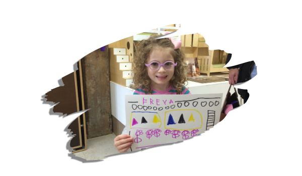 Young girl holding a large educational poster with shapes and patterns, smiling in a showroom.