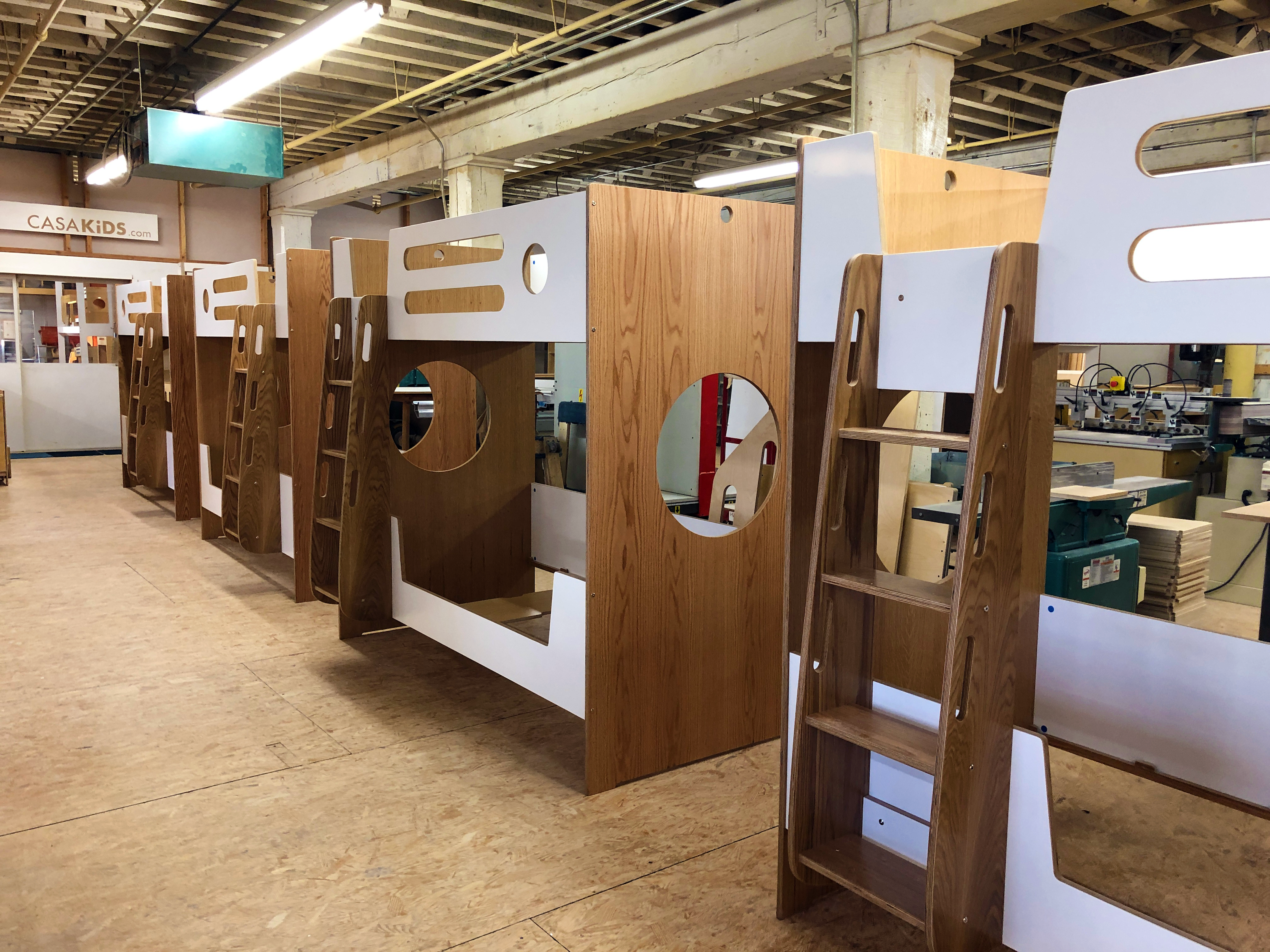 A workshop with a series of unfinished wooden children's bed frames featuring playful cutouts and built-in ladders.