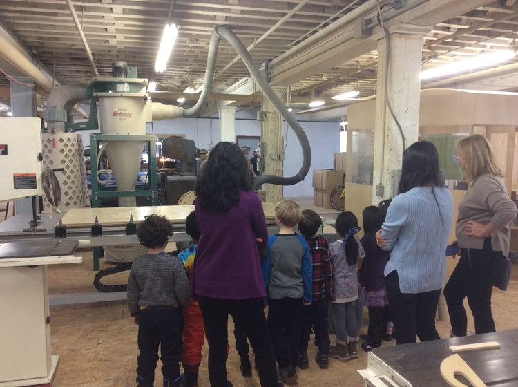 Group of children and adults touring a workshop with large machinery.