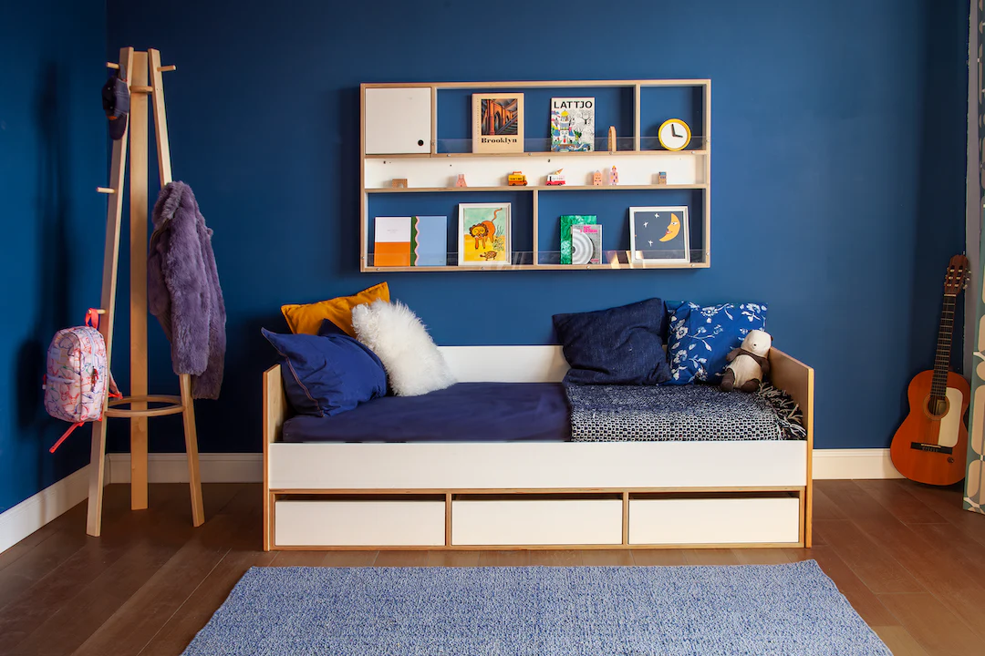 Cozy blue room with bed, shelves, guitar, art supplies, and blue rug.