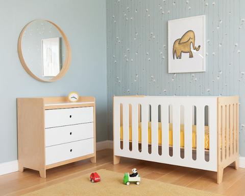 Nursery with a crib, dresser, mirror, toys, and an elephant painting on a patterned wall.
