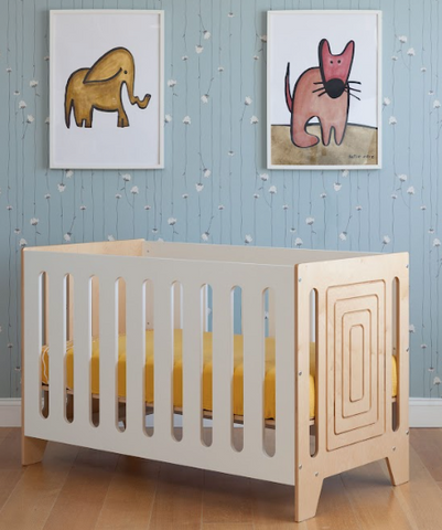 Nursery room with a wooden crib and two framed animal paintings on a patterned wall.