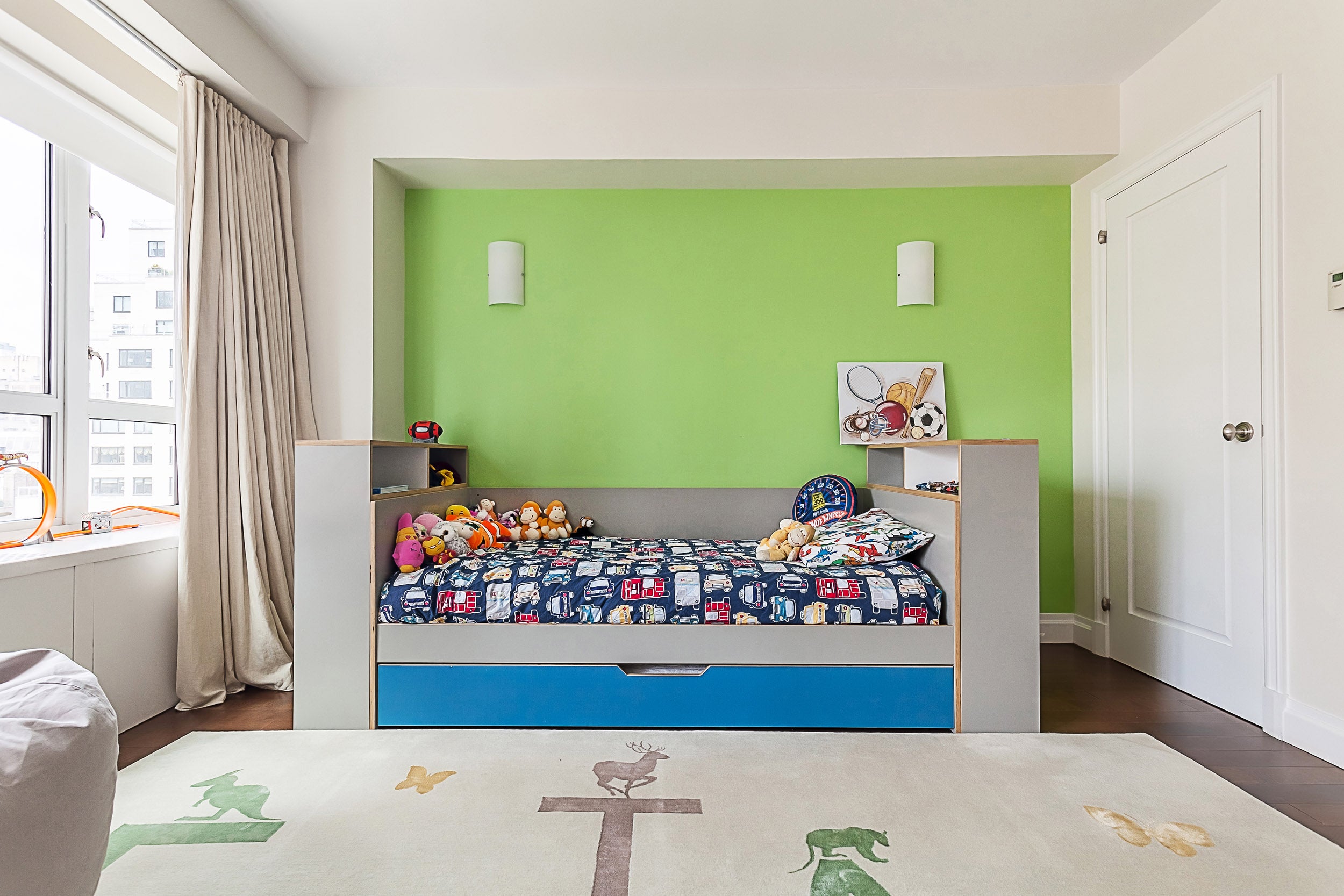 Child's bedroom, green wall, bed with toys, window, carpet.