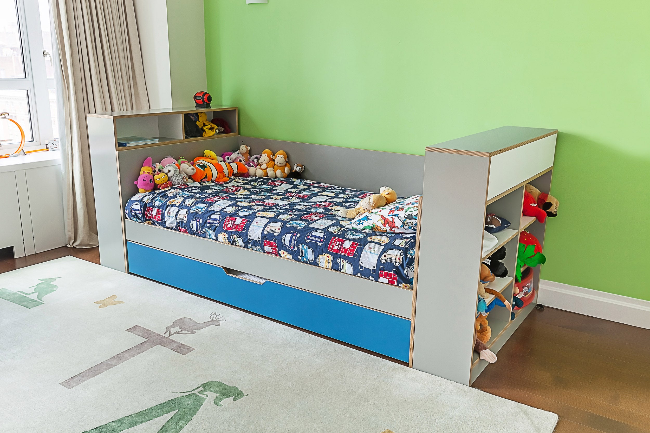 Child’s room with bed, stuffed toys, green wall, animal rug.