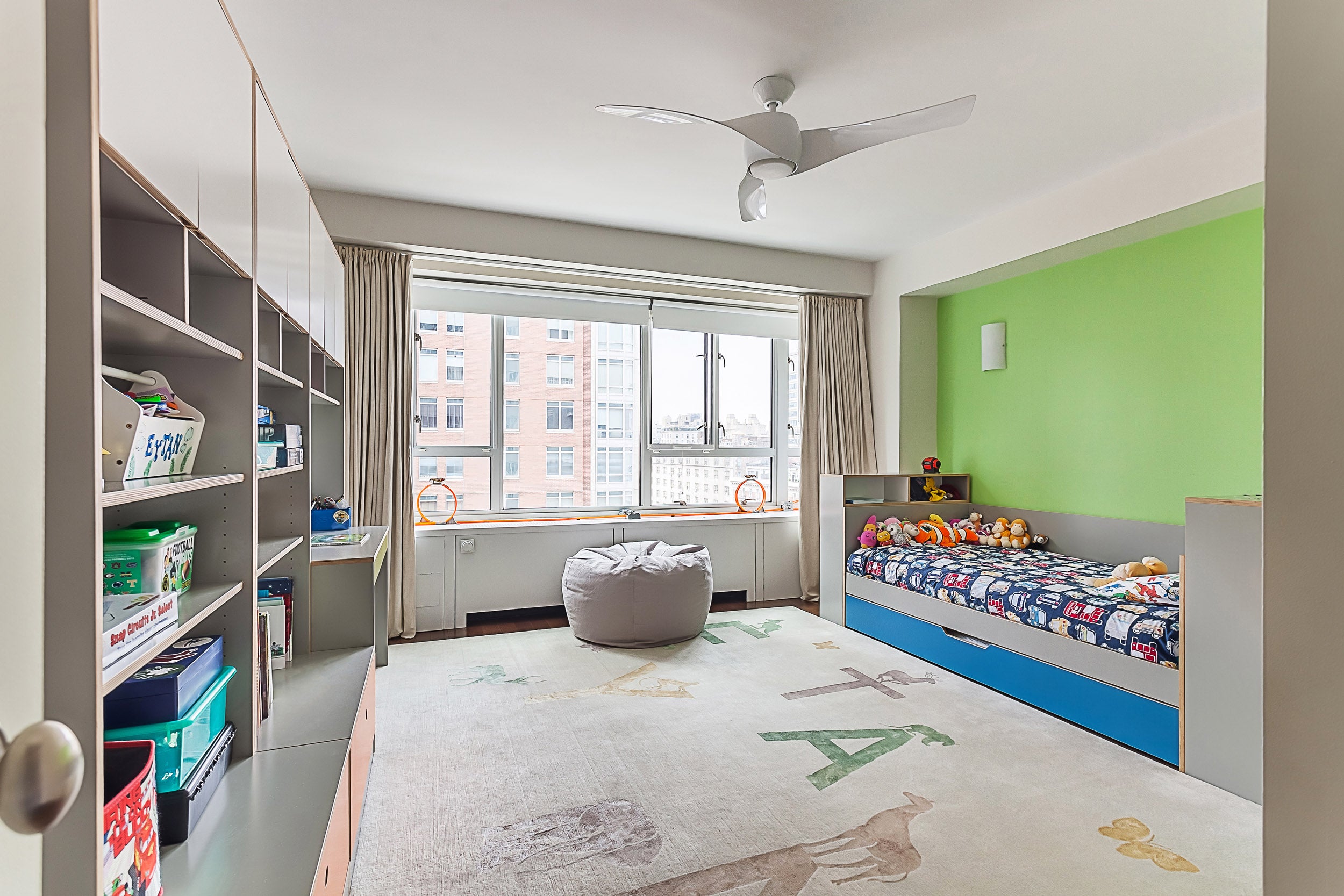 Bright child’s room with green wall, bed, beanbag, rug, and window view