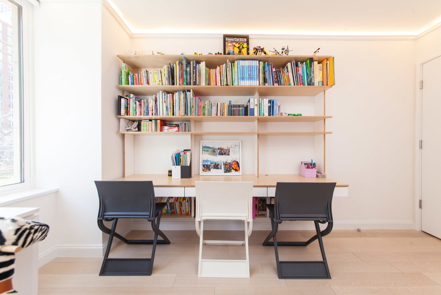 A study room with a white table, two black chairs, and shelves full of books.