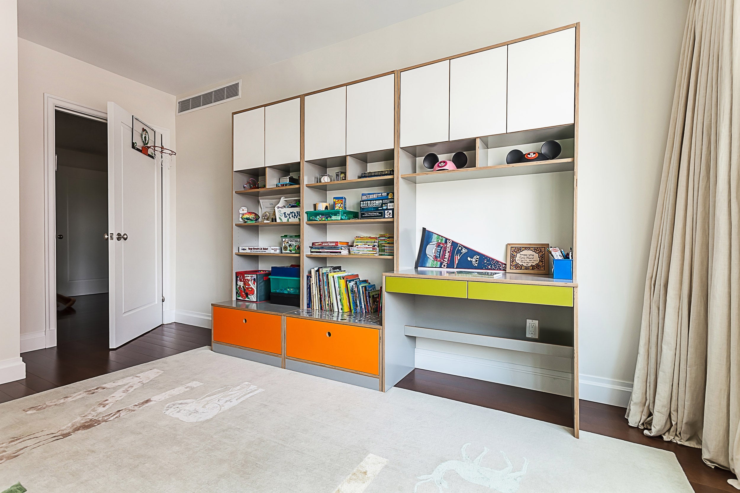 Modern room with white walls, built-in shelf, orange drawers, books, and desk area.