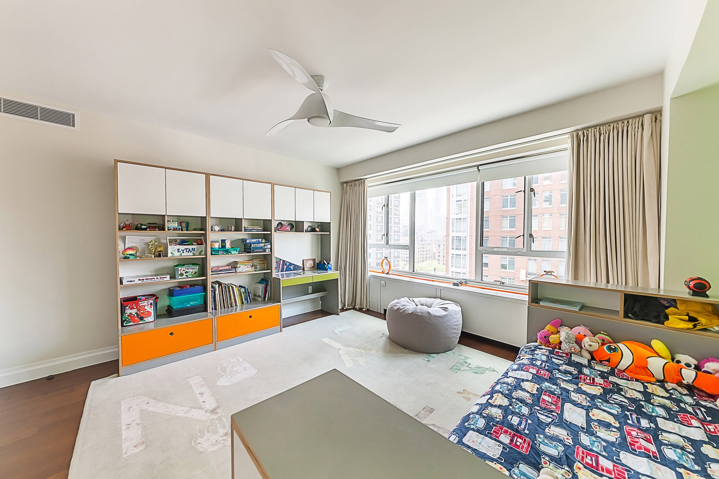 Child’s room with toys, bookshelf, large window, bean bag, and ceiling fan.