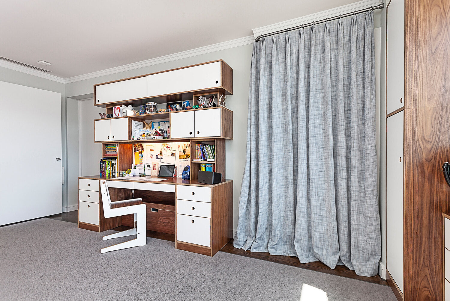 Study room with white desk, bookshelves, and large window with gray curtains.