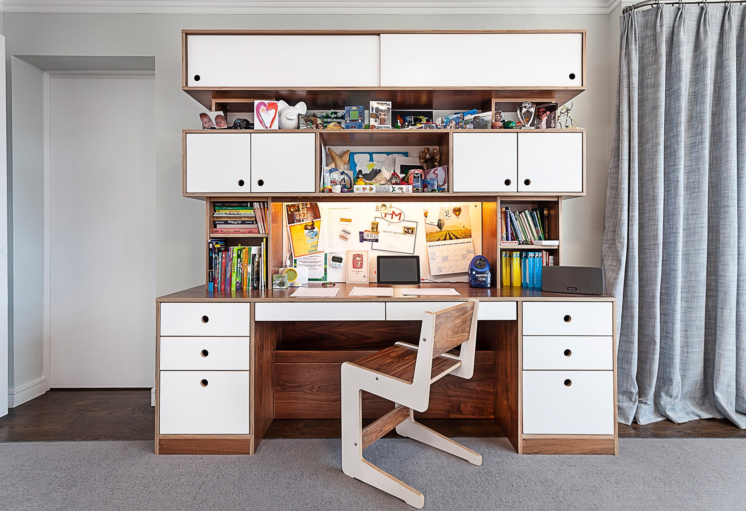 Elegant home office with white desk, matching drawers, shelves filled with books, and a stylish chair.