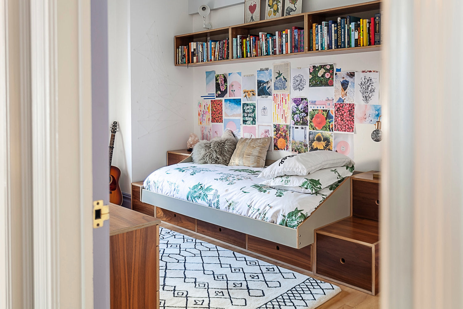 Cozy bedroom with guitar, art wall, bookshelf, and patterned rug.