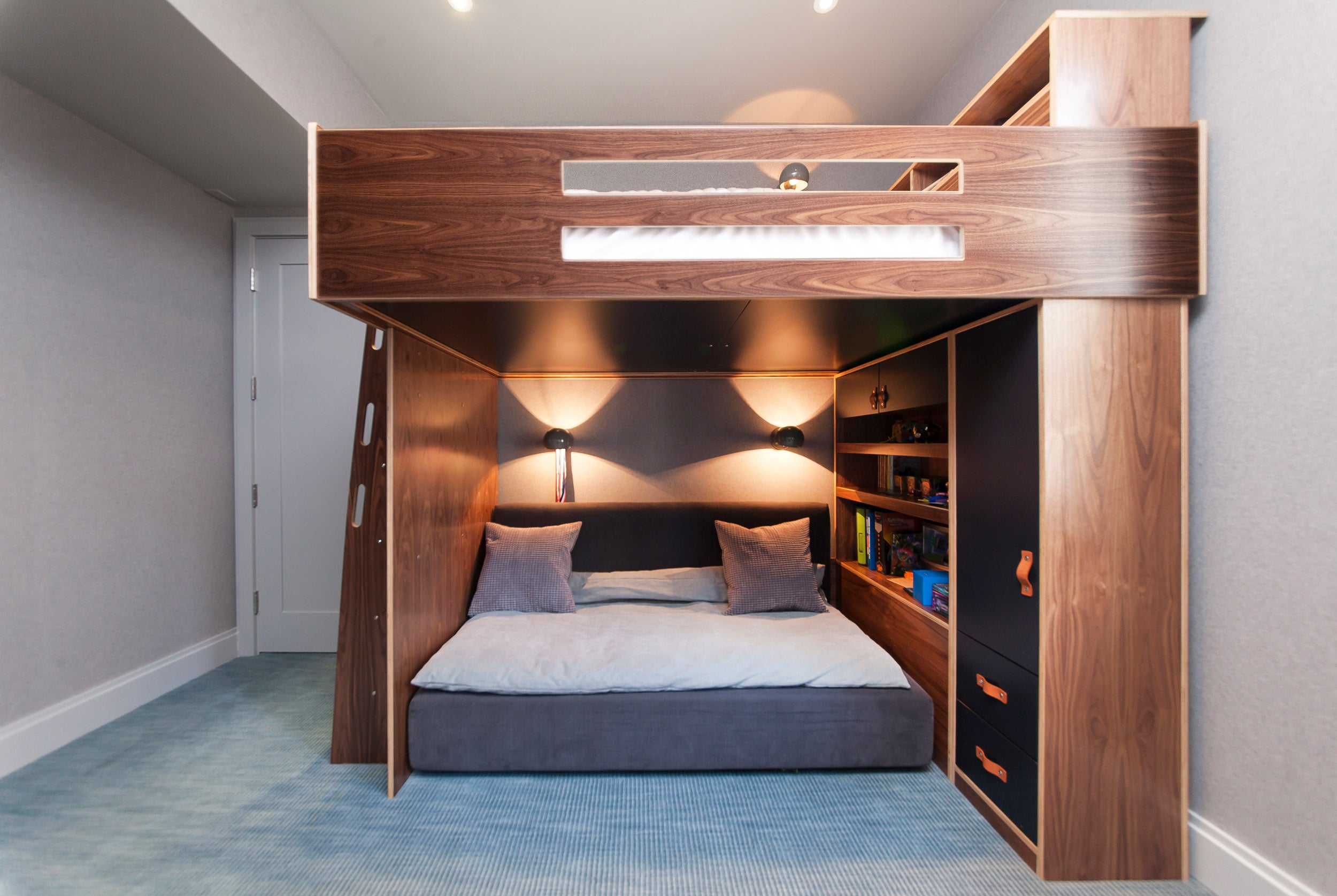 Stylish loft bed with under-bed lighting, built-in shelves, and rich wooden finish in a blue room.