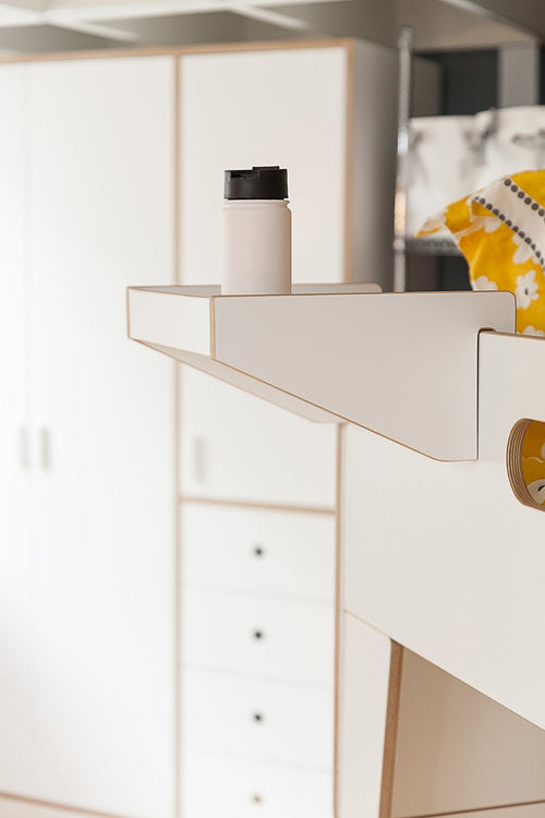 Close-up of a modern white bedside shelf with a thermos, next to a matching white drawer unit.