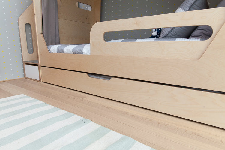 Modern wooden bed frame with a trundle drawer partially visible, set against a striped area rug.