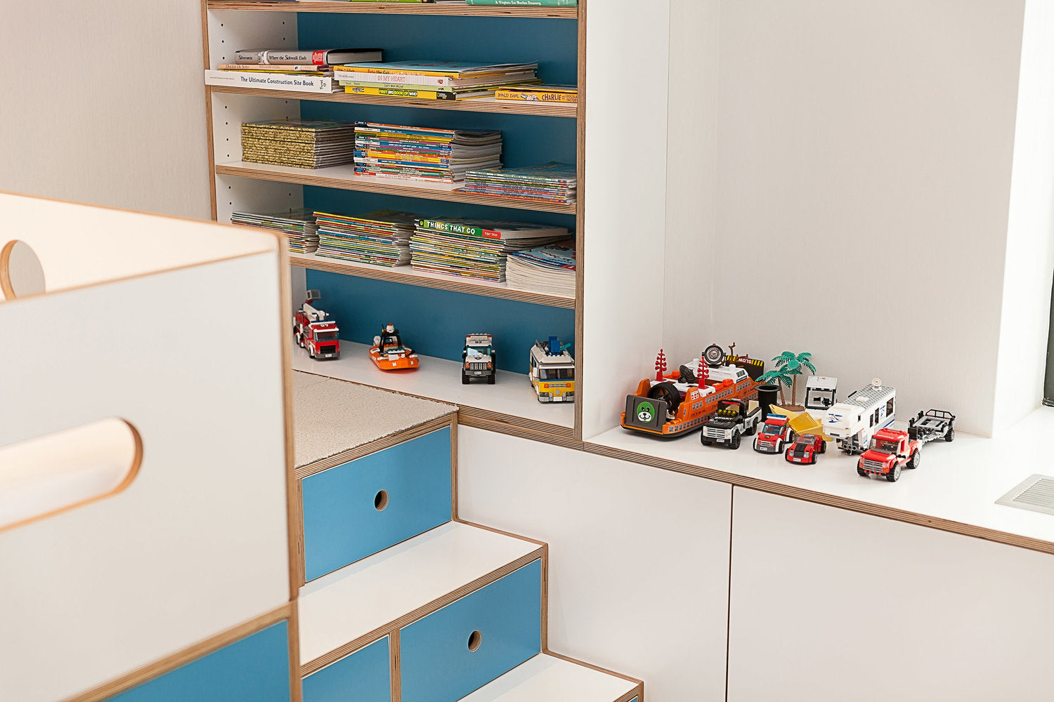 Colorful books and toy vehicles on a bookshelf.