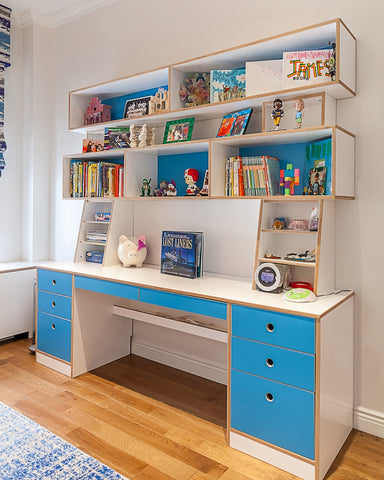 Colorful children's study area with white desk, blue drawers, and floating shelves filled with books.