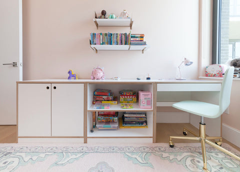 Pastel-themed study space with a modern desk, shelves with books, and a decorative rug in a child's room.