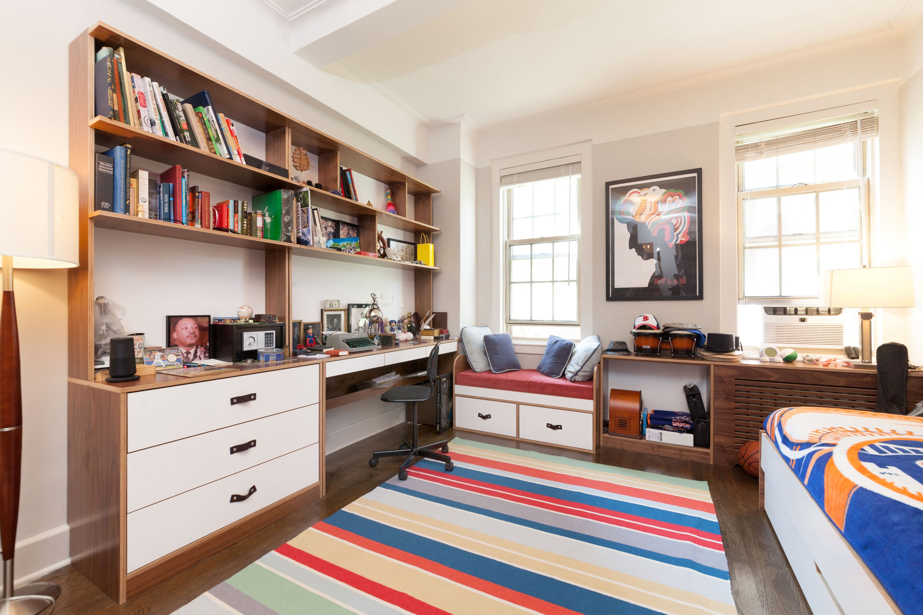 Stylish bedroom with a work desk, bookshelves, a striped rug, and a sports-themed bedspread.