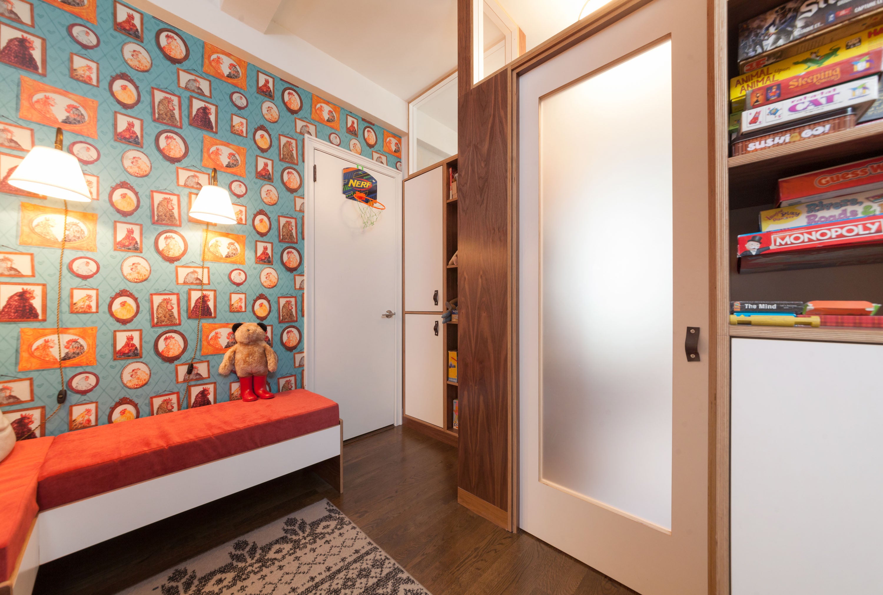 Cozy room with red bed, patterned wallpaper, shelf of games.