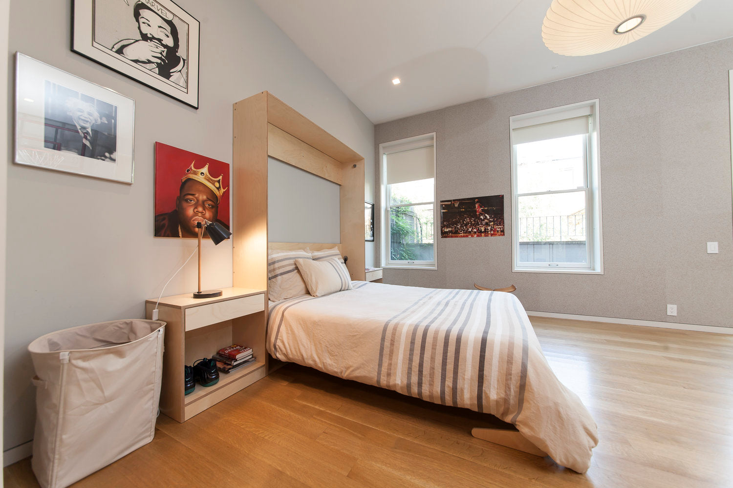 Modern bedroom with bed, side table, lamp, art, and hardwood floor.