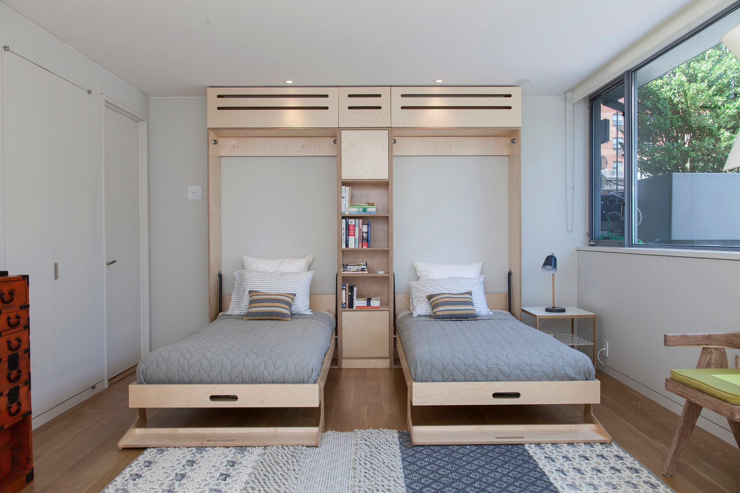 Modern room with twin beds, storage drawers, and shelves, in light wood tones and white.