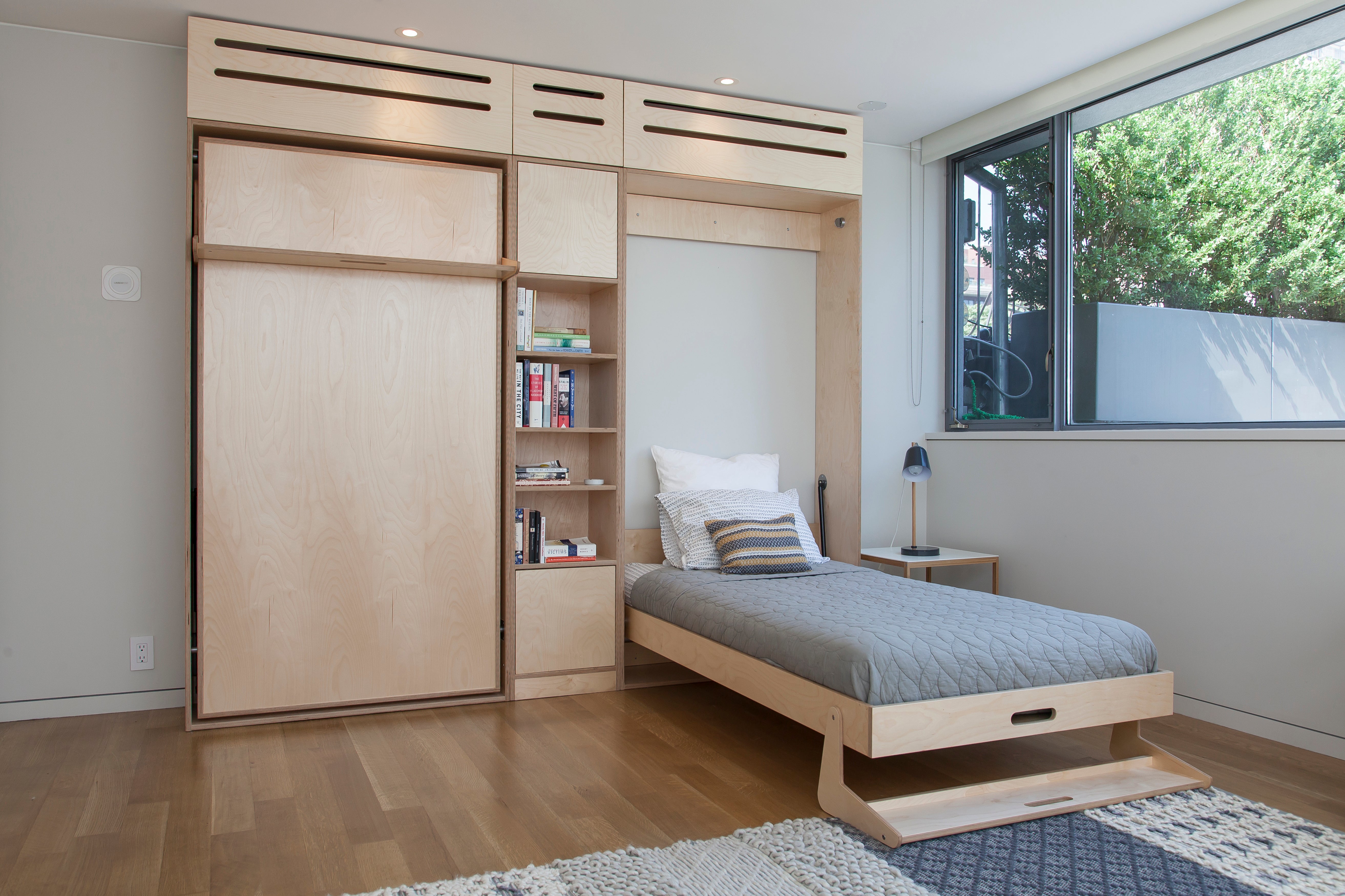 Modern room with a Murphy bed, wooden cabinets, and a large window.