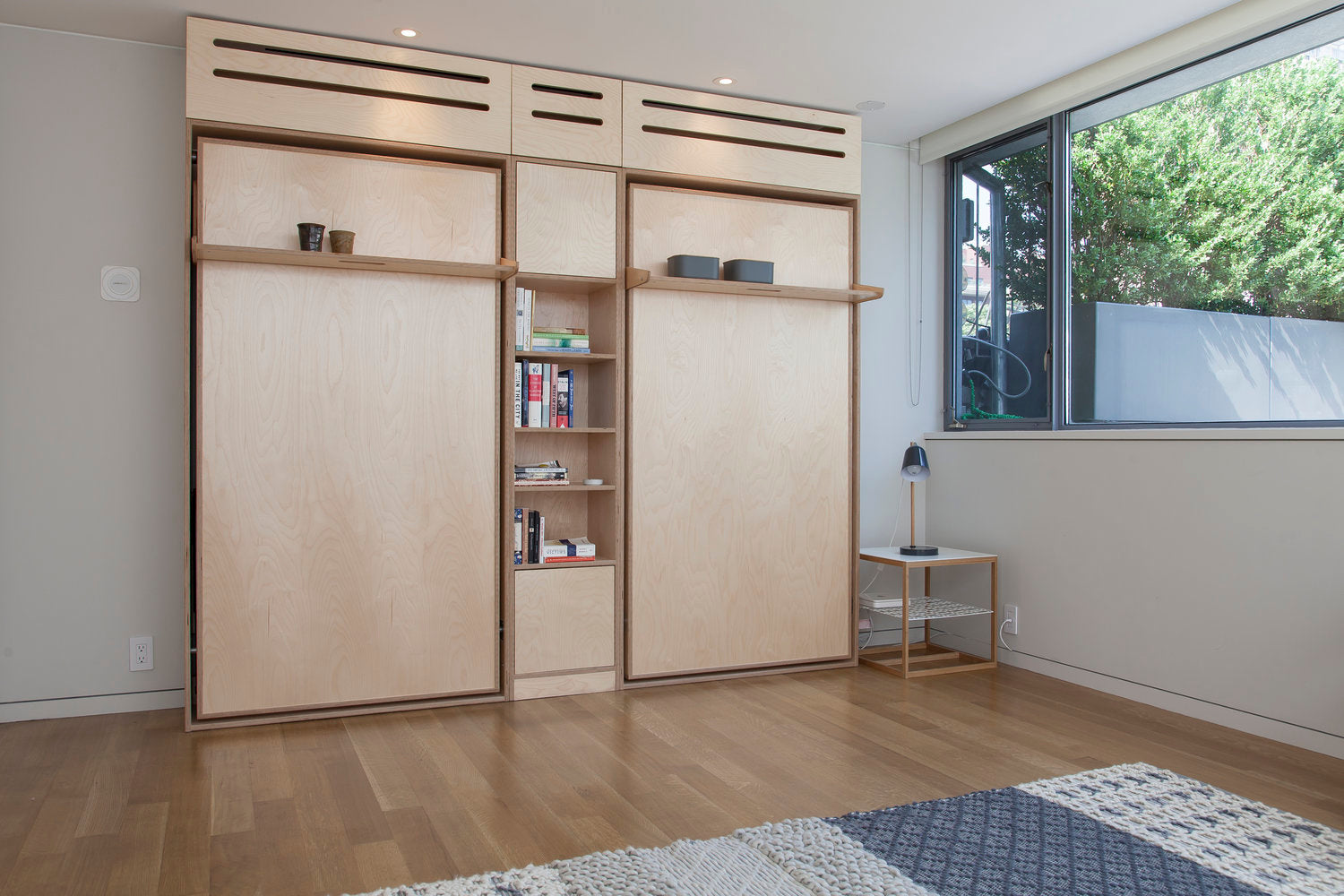 Interior with wooden doors, bookshelf, window, stool, and patterned rug.