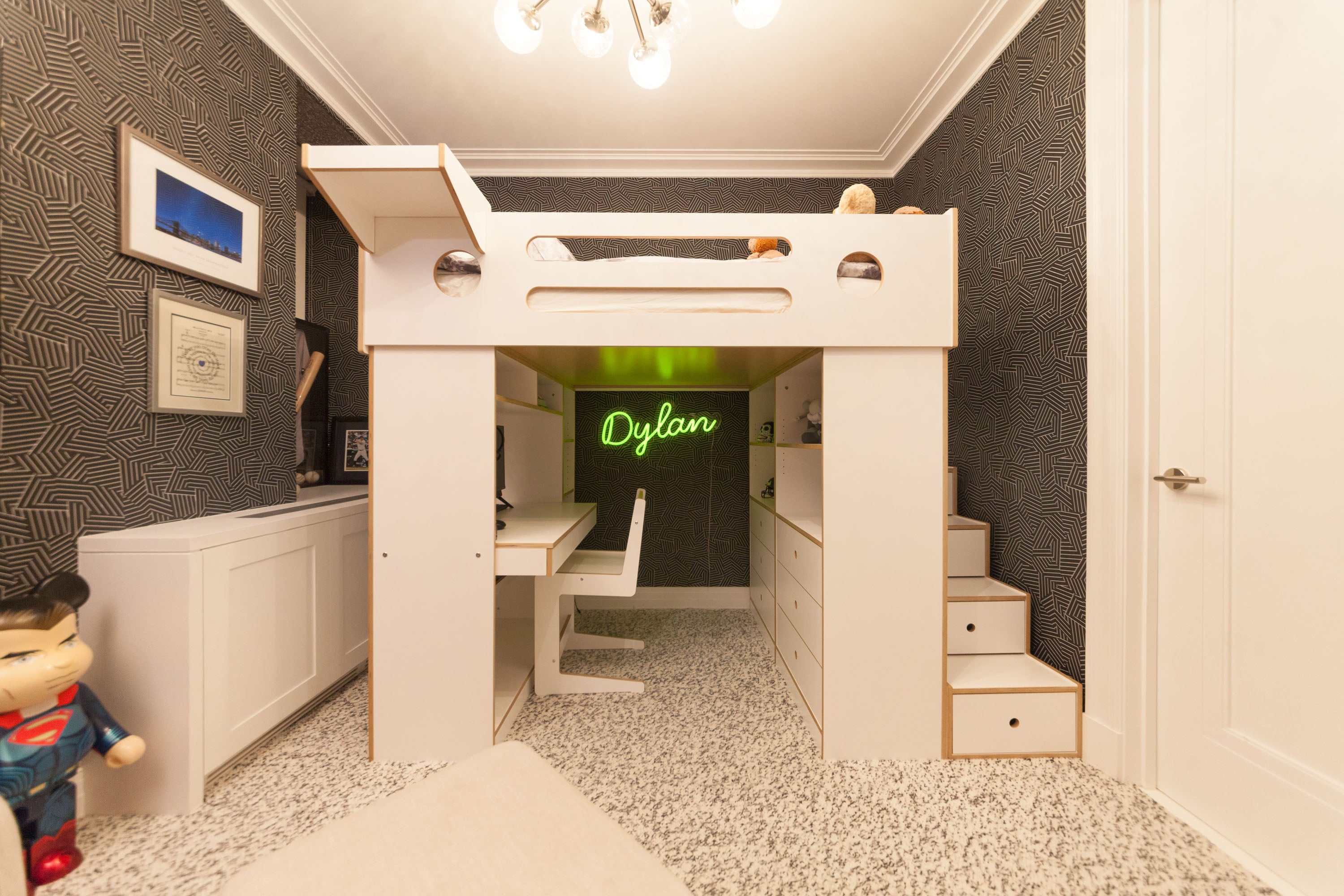 Room with loft bed, desk, “Dylan” neon sign, and patterned wallpaper.