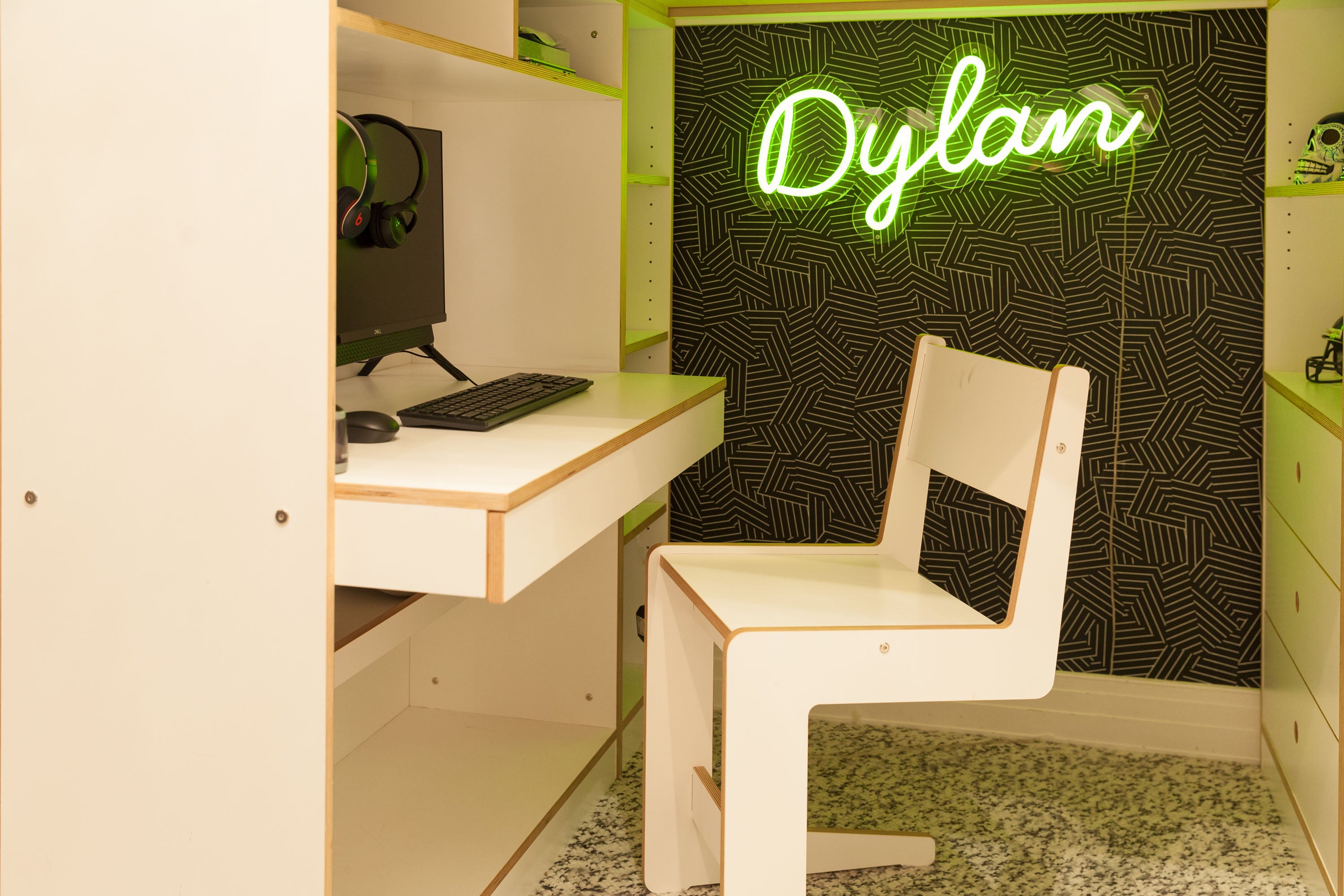 Modern desk, computer, ‘Dylan’ neon sign, patterned wall, white chair.