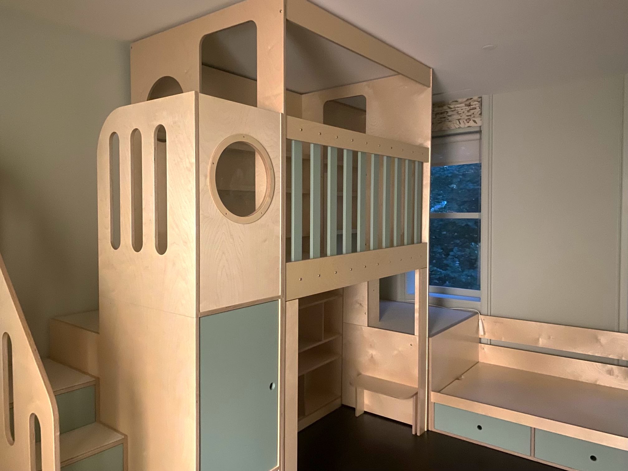 Children's bunk bed in a modern design with pale blue accents and built-in storage, near a window.