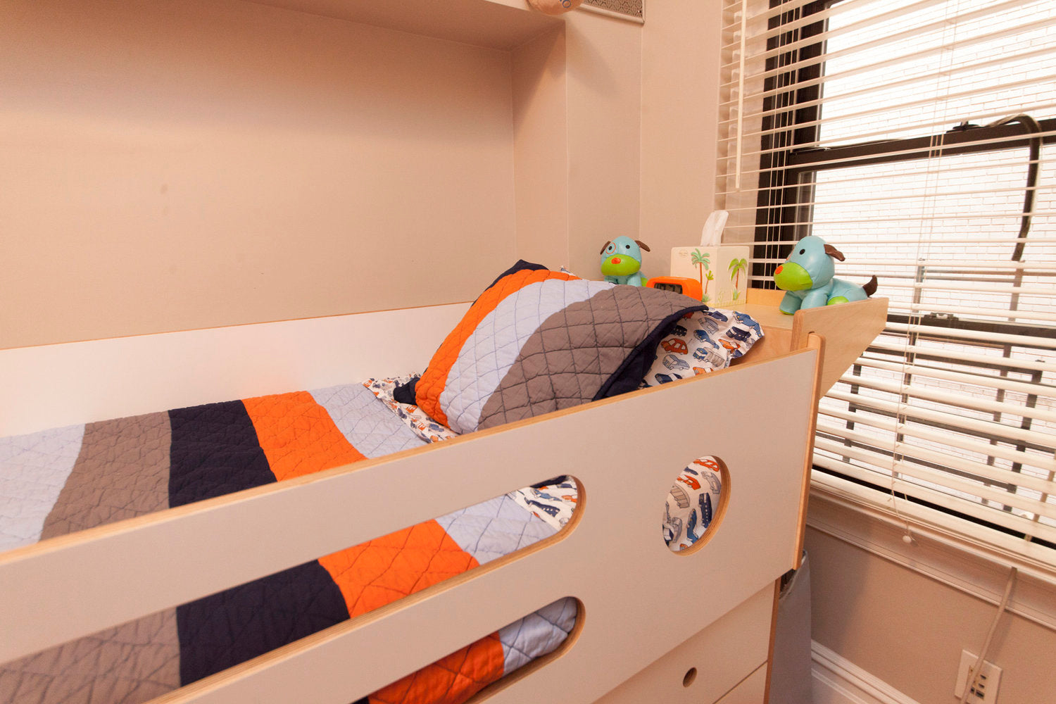 Bunk bed with colorful quilt and plush toys in a room with open blinds.