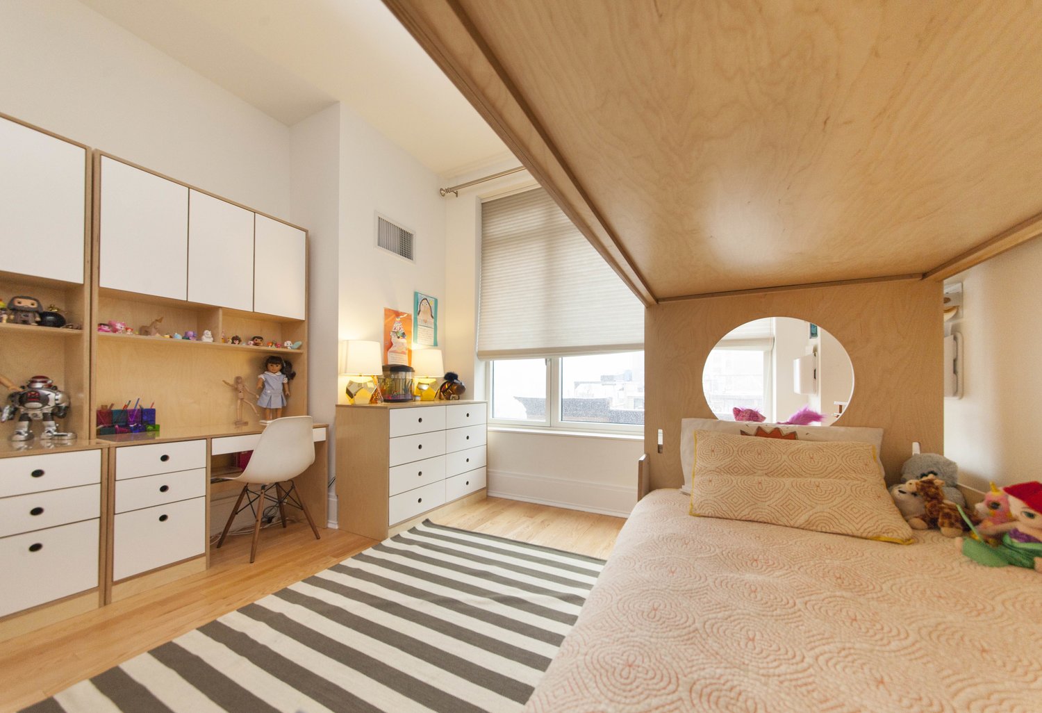 Bright child's room with modern furniture, a striped rug, and a unique window design.
