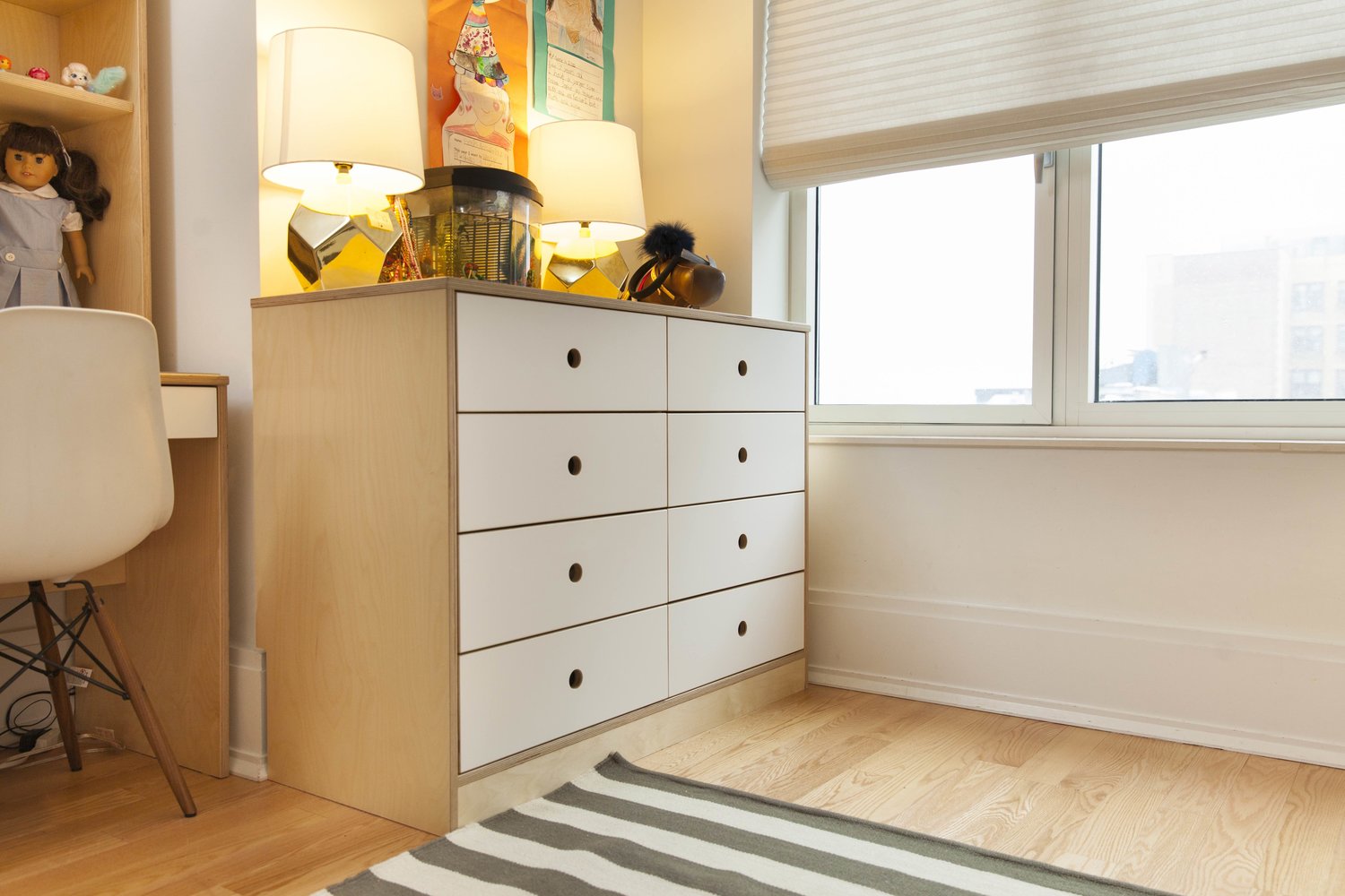 Warmly lit room corner with a modern dresser, desk, and colorful accessories.