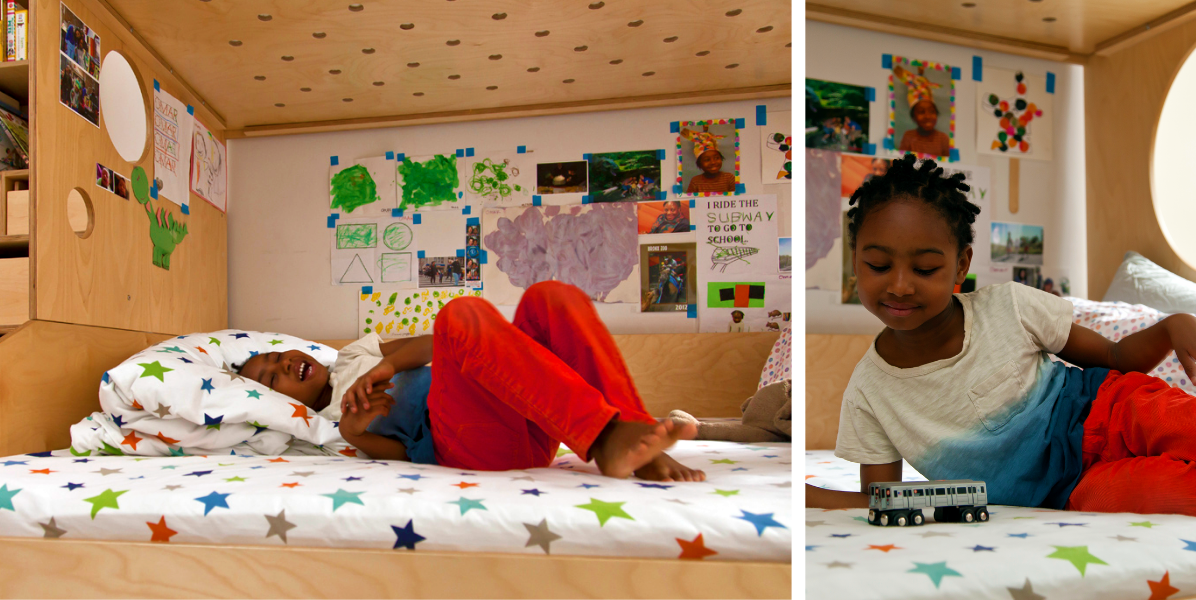 A child in a bed with star-patterned sheets, surrounded by colorful drawings and photos taped to the wall above.