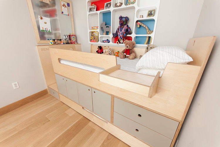 Modern children's bed with storage drawers and a shelf full of toys and books, in a light room.