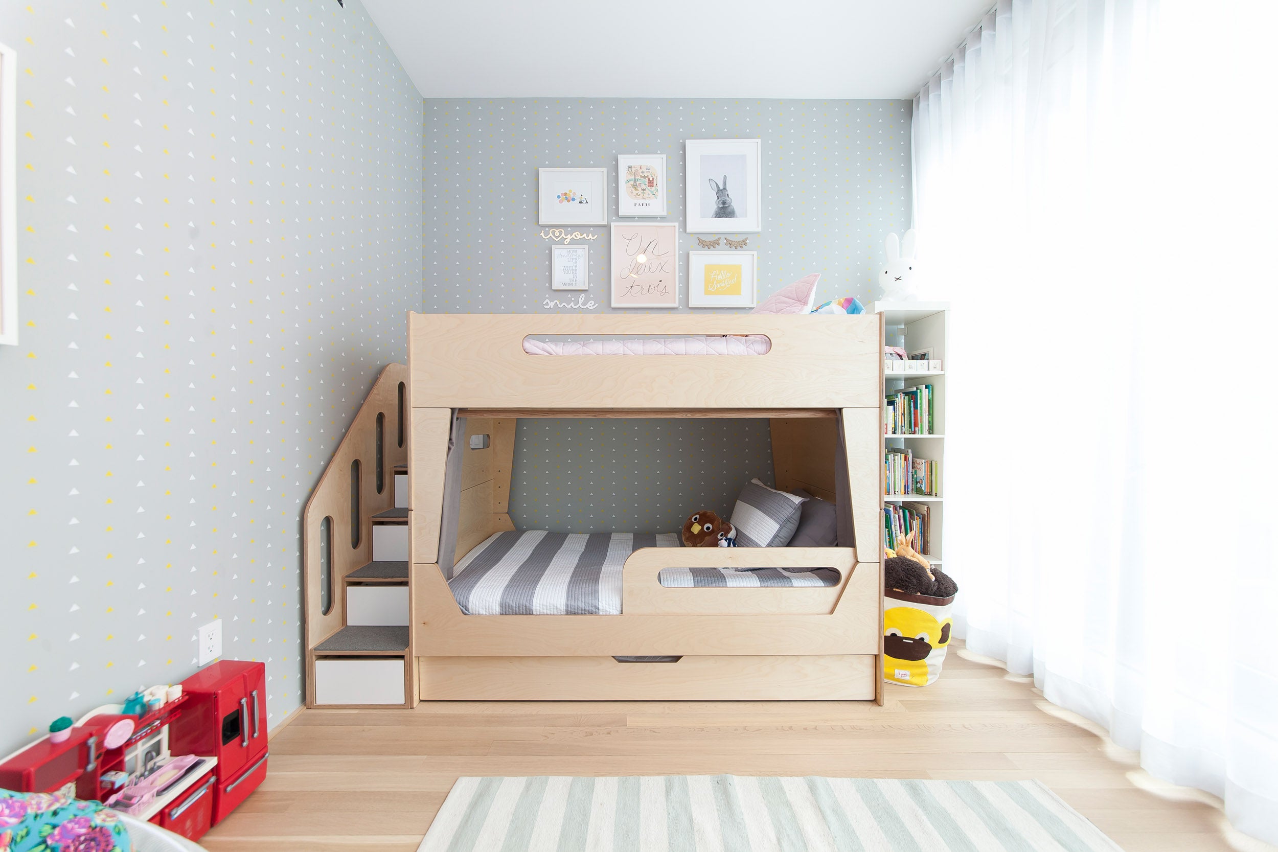 Modern child's room with loft bed, built-in stairs, bookshelf, and light polka-dot wallpaper.