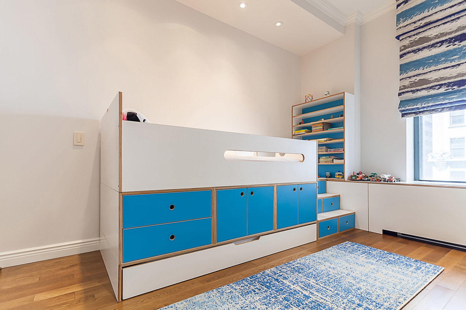 Modern children’s room with blue drawers and patterned rug.