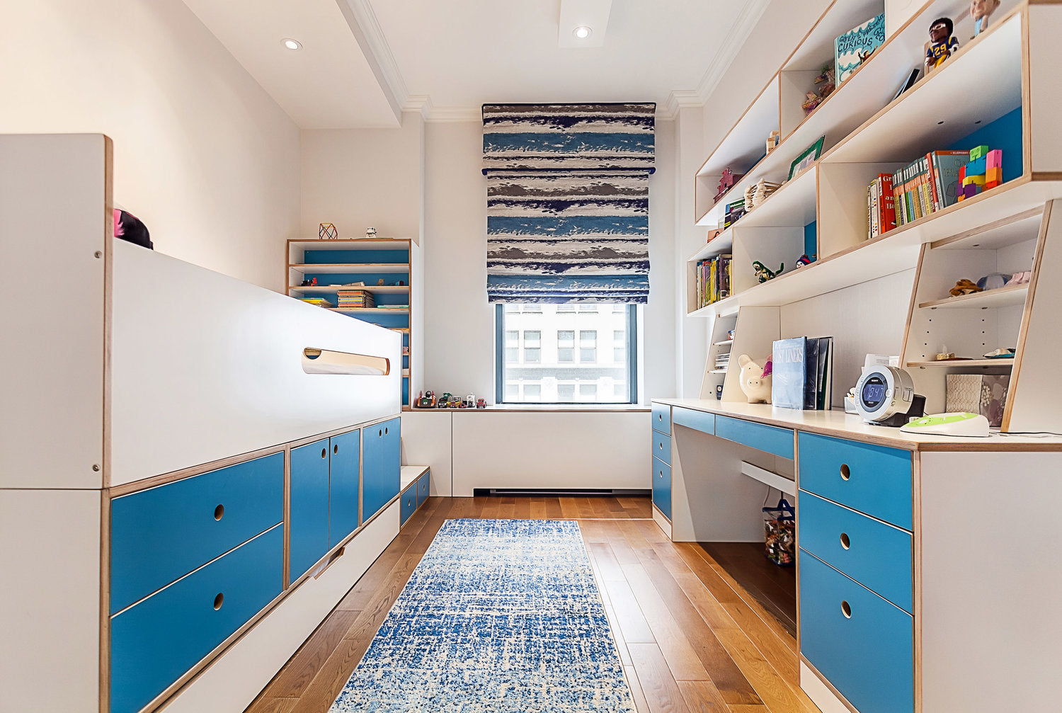 Modern child’s room with blue beds, white shelves, and patterned rug.