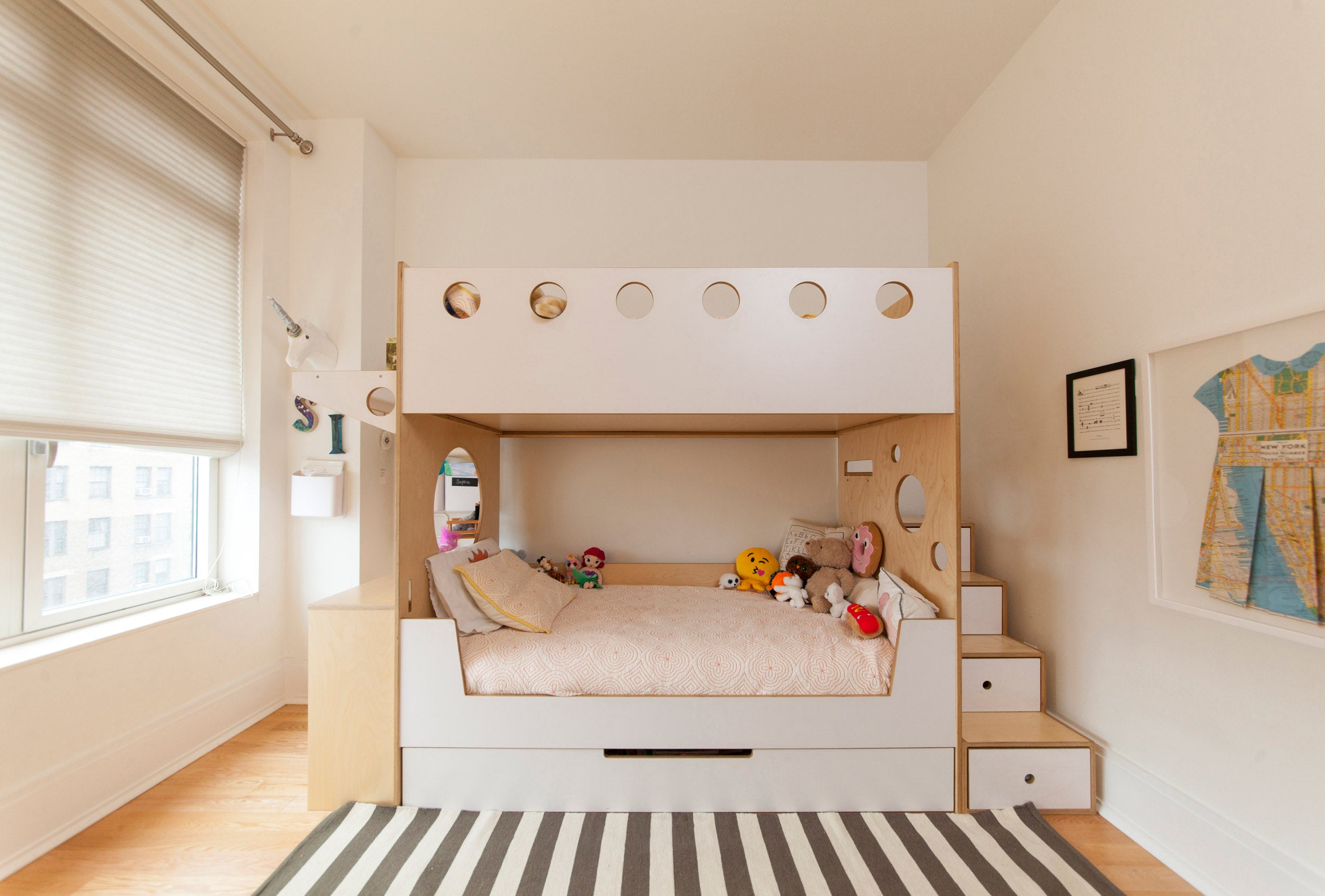 A child's room with a white bunk bed, striped rug, and a world map on the wall, lit by natural light from a window.